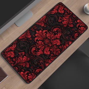 Könnte beinhalten: Eine rechteckige Schreibtischunterlage mit einem sich wiederholenden Damastmuster in leuchtendem Rot und tiefem Schwarz. Das Design besteht aus komplexen, geschwungenen Blumen- und Blattmotiven, die die gesamte Oberfläche der Unterlage bedecken.