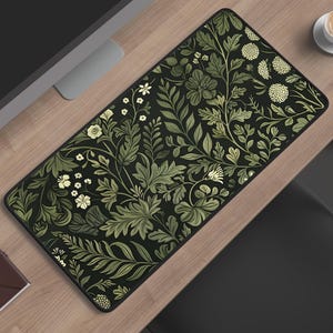 May include: A rectangular desk mat featuring a dark black background with a dense, repeating botanical pattern of light green and cream-colored leaves, ferns, and small round flowers. The mat has a black stitched edge and a smooth, flat surface.