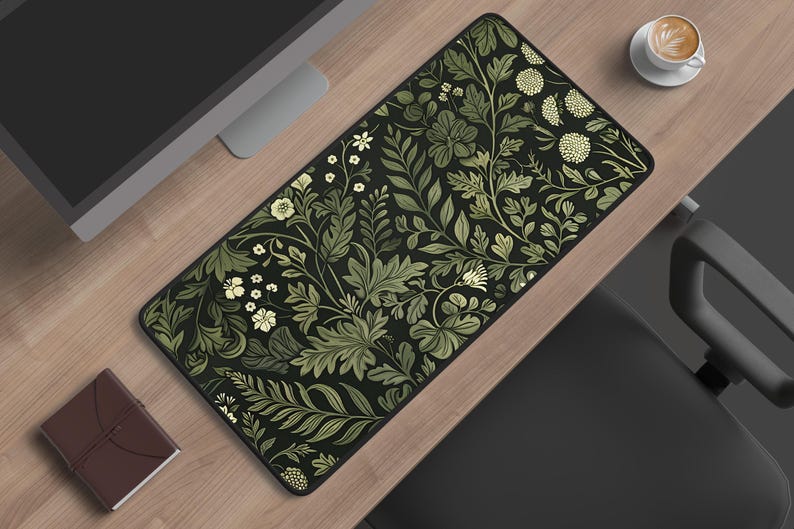 May include: A rectangular desk mat featuring a dark black background with a dense, repeating botanical pattern of light green and cream-coloured leaves, ferns, and small round flowers. The mat has a black stitched edge and a smooth, flat surface.