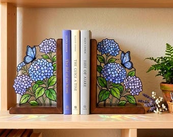 May include: A pair of wooden bookends featuring stained glass panels with blue and purple hydrangea flowers and butterflies. The bookends support three books with spines labeled The Lid of the Worn, The Guice a Tine, and Fine of Aiare.