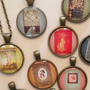 May include: A collection of 15 round glass pendants with bronze chains. Each pendant features a vintage book cover illustration. The book titles include "Moby Dick", "The Secret Garden", "The Tale of Peter Rabbit", "Treasure Island", "The Adventures of Tom Sawyer", "Anne of Green Gables", "The Wind in the Willows", "A Little Princess", "The Jungle Book", "Black Beauty", "The Railway Children", "The Adventures of Sherlock Holmes", "The Call of the Wild", "The Wonderful Wizard of Oz", and "The Adventures of Huckleberry Finn".