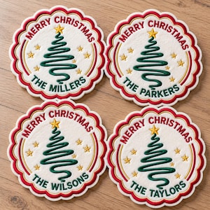 May include: Four round, scalloped-edge coasters with a white center and red border. Each features an embroidered green spiral Christmas tree topped with a gold star, surrounded by small gold stars. Text reads MERRY CHRISTMAS and family names.