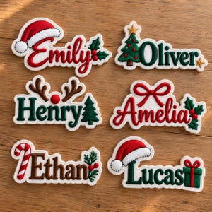 May include: Six embroidered Christmas-themed name patches featuring the names Emily, Oliver, Henry, Amelia, Ethan, and Lucas. Each patch includes festive icons like a Santa hat, a Christmas tree, reindeer antlers, a bow, a candy cane, and a gift.