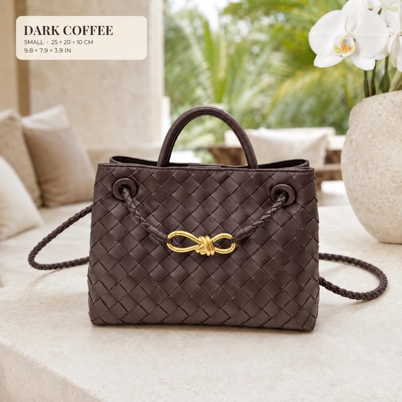 K&ouml;nnte beinhalten: Eine dunkelkaffeebraune Handtasche mit geflochtenem Lederau&szlig;enmaterial, zwei Tragegriffen und einem geflochtenen Schulterriemen. Die Vorderseite ist mit einem goldfarbenen Metallknoten verziert. Die Tasche misst 25 x 20 x 10 cm laut Bild.