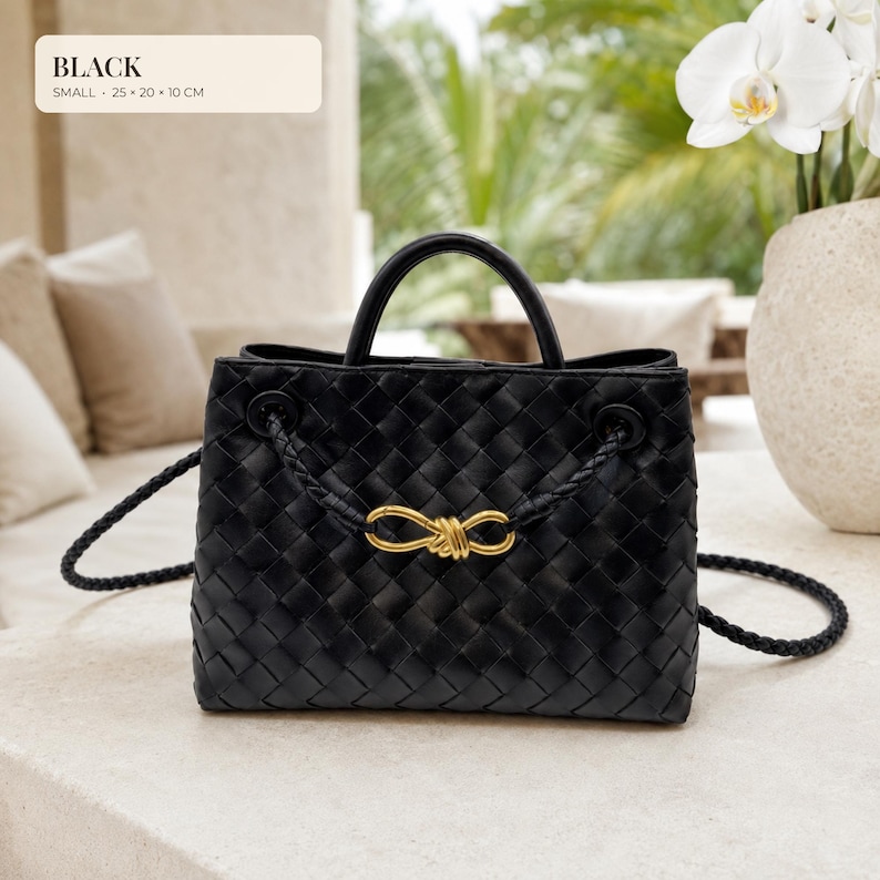 K&ouml;nnte beinhalten: Eine schwarze geflochtene Handtasche mit einem goldenen Knotendetail auf der Vorderseite. Die Tasche hat zwei Tragegriffe und einen geflochtenen Schulterriemen. Der Text auf dem Bild lautet: BLACK, SMALL, 25 x 20 x 10 CM. Das Muster ist gitterartig.