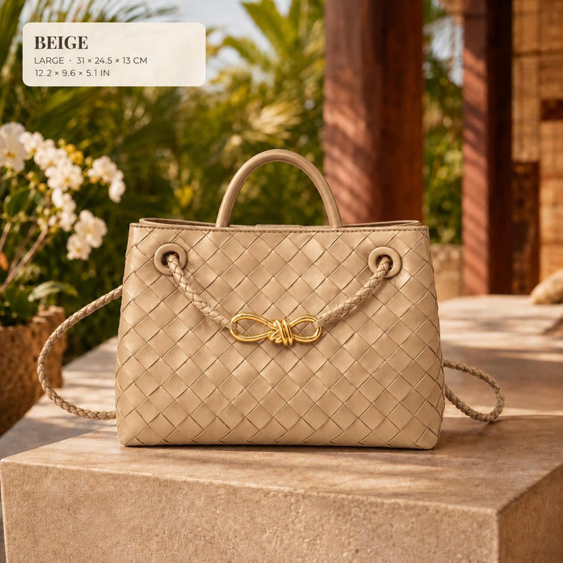 K&ouml;nnte beinhalten: Eine beige geflochtene Ledertasche mit einem strukturierten Tragegriff und einem geflochtenen Schulterriemen mit einer goldfarbenen Metallschleife. Die Tasche misst 31 x 24,5 x 13 cm, wie im Text auf dem Bild angegeben.