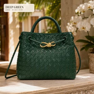 K&ouml;nnte beinhalten: Eine dunkelgr&uuml;ne geflochtene Handtasche mit einem strukturierten Tragegriff und einem goldfarbenen Knotenverschluss. Die Tasche hat einen geflochtenen Schulterriemen und misst 31 x 24,5 x 13 cm. Der Text DEEP GREEN und die Ma&szlig;e stehen oben links.
