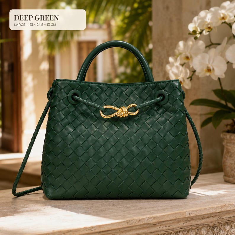 K&ouml;nnte beinhalten: Eine dunkelgr&uuml;ne geflochtene Handtasche mit einem strukturierten Tragegriff und einem goldfarbenen Knotenverschluss. Die Tasche hat einen geflochtenen Schulterriemen und misst 31 x 24,5 x 13 cm. Der Text DEEP GREEN und die Ma&szlig;e stehen oben links.