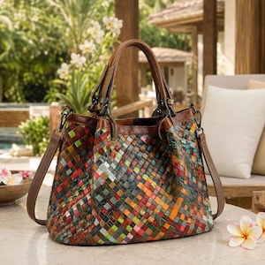 Puede incluir: Un bolso de mano de cuero trenzado multicolor con un diseño de patrón cuadrado en tonos rojo, verde, azul, naranja y amarillo. El bolso incluye asas de cuero marrón, una correa de hombro marrón desmontable y herrajes de metal oscuro.