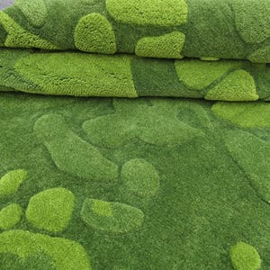 May include: A plush area rug featuring a textured, tufted surface with an organic, irregular pattern of overlapping shapes in varying shades of lime green and forest green. The rug is folded over, revealing a dense, soft pile and a consistent color palette.