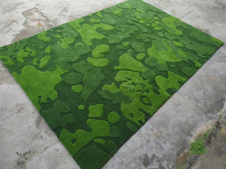 May include: A rectangular area rug featuring a textured, carved surface with an abstract camouflage pattern in various shades of green. The design consists of organic, irregular shapes in light lime and deep forest green tones with pile height.