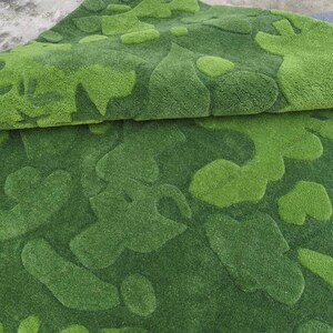 May include: A plush area rug featuring a layered, tufted texture in varying shades of green. The surface displays an abstract, organic pattern of raised, rounded shapes in light lime green set against a darker forest green background.