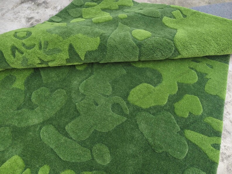 May include: A plush area rug featuring a layered, tufted texture in varying shades of green. The surface displays an abstract, organic pattern of raised, rounded shapes in light lime green set against a darker forest green background.