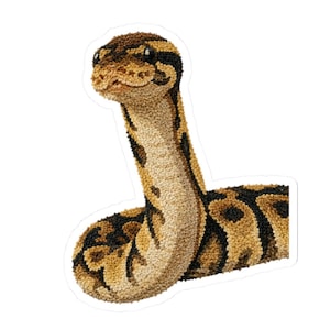 May include: A textured punch needle art piece depicting a ball python snake with a tan and brown patterned body and a cream-coloured underbelly. The snake is shown in an upright, alert posture with its head raised and body coiled at the base.