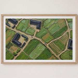 May include: An oil painting in a light wood frame depicting an aerial view of a rural landscape with green fields, dirt paths, and several dark-roofed buildings. The textured brushstrokes create a mosaic of varying shades of green and brown.