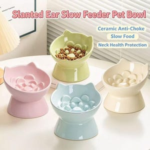 Puede incluir: Cuatro cuencos de cerámica para mascotas con bordes en forma de orejas de gato y patrones internos elevados para ralentizar la alimentación. Los cuencos son de color rosa pastel, verde claro, azul claro y crema. El texto dice Slanted Ear Slow Feeder.