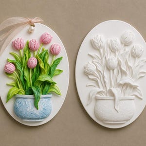 May include: Two oval wall plaques featuring relief sculptures of tulips in pots. One plaque displays pink tulips with green leaves in a light blue pot, accented by a sheer peach ribbon. The second plaque is entirely white, showing the same floral design.