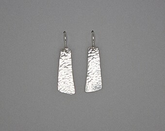 May include: A pair of silver dangle earrings with a hammered texture. The earrings are rectangular in shape and have a slightly curved edge.