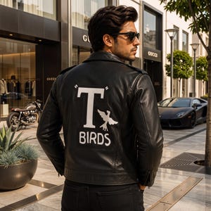 Könnte beinhalten: Eine schwarze Lederjacke mit einem großen weißen Aufnäher auf dem Rücken, der den Buchstaben T, die Silhouette eines Vogels und den Text BIRDS zeigt. Die Jacke hat einen klassischen Kragen, lange Ärmel mit Reißverschlussbündchen und eine glatte Oberfläche.