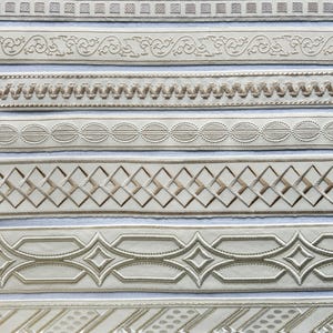 Könnte beinhalten: Eine Sammlung von acht verschiedenen dekorativen Stoffbändern, die horizontal angeordnet sind. Jedes Band weist ein einzigartiges Webmuster in Creme-, Beige- und Hellbrauntönen auf, das geometrische Formen, Ranken und komplexe Ränder zeigt.