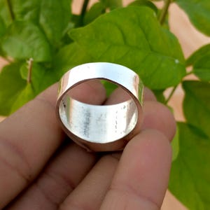 May include: A wide, polished silver-toned band ring with a smooth, reflective surface. The ring features a thick, solid construction with a circular opening, showcasing a metallic finish that catches the light across its entire outer circumference.