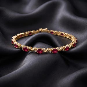 May include: A gold bracelet featuring a series of oval-cut red rubies alternating with small round white diamonds. The metal links have a curved, S-shaped design connecting each gemstone setting, and the piece includes a secure box clasp closure.