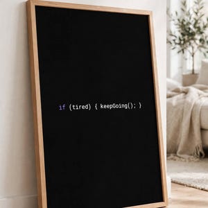 May include: A rectangular framed wall art piece featuring a black background with white programming code text that reads: if (tired) { keepGoing(); }. The frame is made of light-colored wood and is positioned vertically against a white wall.