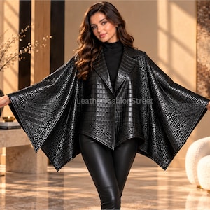 May include: A black leather cape featuring a textured crocodile skin pattern, a wide lapel collar, and an open front design. The garment has a structured bodice with wide, flowing sleeves that extend outward, and the text LeatherFashionStreet is visible.