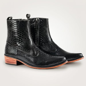 May include: A pair of black ankle boots featuring a glossy snakeskin-embossed texture, a side zip closure, a pull tab at the heel, and a stacked wooden heel with a natural light brown finish and a thin orange accent layer along the sole.
