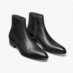 May include: A pair of black ankle boots featuring a textured snakeskin pattern across the exterior. These boots have a pointed toe, a low block heel, and a vertical zip closure on the inner side of each boot, extending from the sole to the ankle.