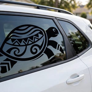 May include: A black vinyl decal of a sea turtle applied to the rear passenger window of a white vehicle. The turtle design features intricate geometric patterns, including triangles and swirling wave-like lines on its shell and flippers.