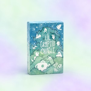 May include: A rectangular deck of cards in a blue and green box with a watercolor forest illustration. The text reads Lil Cryptid Oracle by Ariela. White silhouettes of various small creatures are scattered throughout the foliage design.