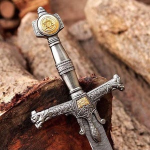 Op de afbeelding: Een decoratief zwaard met een zilverkleurig gevest met ingewikkeld metaalwerk, een goudkleurig embleem van de Davidsster op de pommel, en een pareerstang versierd met gebeeldhouwde leeuwenkoppen en goudkleurige accenten, boven een metalen lemmet.