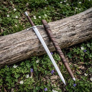 May include: A double-edged steel sword with a brown leather-wrapped handle and a matching brown leather scabbard featuring a spiral leather wrap. The sword has a straight crossguard and a pointed tip, resting alongside its protective sheath.
