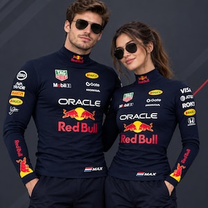 May include: A dark navy blue long-sleeve mock neck shirt featuring the Oracle Red Bull Racing logo, two red bulls, and various sponsor logos including Tag Heuer, Mobil 1, Honda, and Esso. The shirt includes the text MAX and a small Dutch flag.