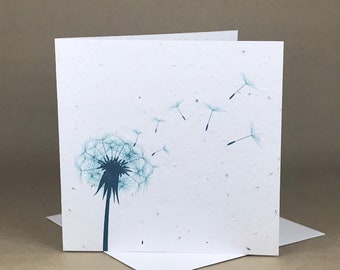 May include: A white card with a blue dandelion design. The dandelion is blowing in the wind and the seeds are floating away. The card is made of recycled paper and has a speckled texture.