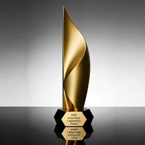 May include: A tall, gold-coloured trophy featuring a smooth, curved, flame-like structure rising from a black hexagonal base. The base displays the text 2025 Innovation Leadership Award in black lettering, with a clear reflection visible below.