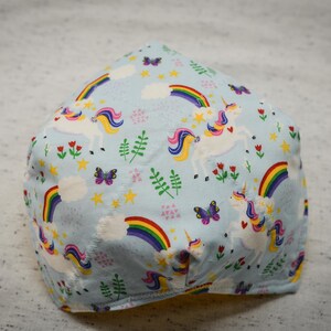 May include: A light blue fabric face mask with a repeating pattern of white unicorns, rainbows, butterflies, and stars.