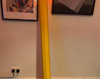 Peut inclure: Un grand lampadaire en forme de crayon jaune géant. Le corps est hexagonal et jaune, avec une virole en métal argenté près du sommet. La pointe du crayon émet une lumière orange vive et chaude, imitant l'apparence d'une flamme.