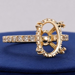 May include: A yellow gold ring setting featuring an oval-shaped center mount with prongs designed to hold a gemstone. The band and the outer edge of the center mount are encrusted with small, round, clear pavé-set stones along the entire visible shank.