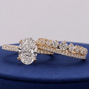 Op de afbeelding: Een gouden ringenset bestaande uit een verlovingsring met een ovaal geslepen middensteen en een pavé gezette diamanten band, gecombineerd met een bijpassende gouden trouwring met een rij briljant geslepen diamanten en een fijn pavé detail.