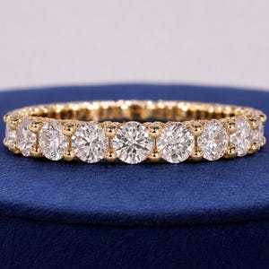 Könnte beinhalten: Ein Ewigkeitsring aus Gelbgold mit einer durchgehenden Reihe runder, im Brillantschliff geschliffener, klarer Steine in einer gemeinsamen Krappenfassung. Der Ring zeigt eine gleichmäßige Anordnung funkelnder Steine um den gesamten Ringumfang.