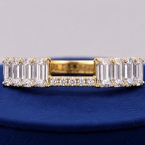 Könnte beinhalten: Ein Ring aus goldfarbenem Metall mit zwei Abschnitten aus vertikalen Baguette-geschliffenen klaren Steinen und einer Verbindungsbrücke, die mit einer Reihe kleiner runder klarer Steine besetzt ist. Der Ring hat eine polierte Oberfläche.