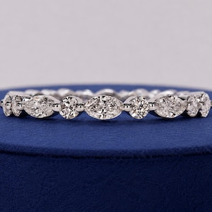 Könnte beinhalten: Ein silberfarbener Eternity-Ring mit einem abwechselnden Muster aus marquise- und rundgeschliffenen klaren Steinen in einer durchgehenden Reihe. Das Metallband hat eine polierte Oberfläche und die Steine bilden ein sich wiederholendes, symmetrisches Design.