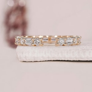 Könnte beinhalten: Ein offener Goldring mit einem abwechselnden Muster aus runden Brillantschliff-Steinen und rechteckigen Baguetteschliff-Steinen entlang der Ringschiene. Der Ring hat eine polierte Goldoberfläche und eine Lücke in der Mitte des Designs.