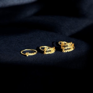 May include: Three gold-toned rings featuring cursive script lettering. The first ring displays the name Grace, the second ring features the names May and Sarah, and the third ring displays the names Maya, Hailey, and Sarah in a stacked design.