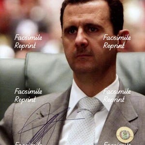 Puede incluir: Retrato de un hombre con cabello oscuro y bigote, vistiendo un traje gris, camisa blanca y corbata gris claro. Un pin circular está sujeto a la solapa izquierda. La imagen presenta una firma y el texto repetido Facsimile Reprint.