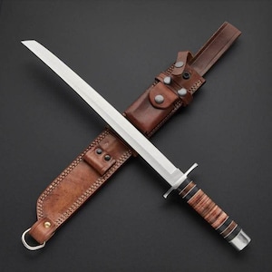 Puede incluir: Un cuchillo de hoja fija con una hoja de acero plateado y un mango que presenta anillos de cuero marrón apilados con espaciadores negros. El cuchillo está colocado en diagonal sobre una funda de cuero marrón con un anillo en D y broches.