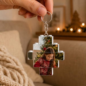 Puede incluir: Un llavero personalizado hecho de bloques de construcción de plástico entrelazados, con una fotografía impresa de una persona con un suéter rojo estampado frente a un árbol de Navidad decorado. Incluye una anilla de metal plateado.