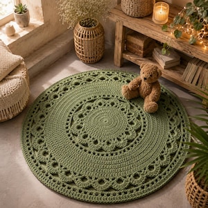 May include: A round, sage green crochet rug featuring a central spiral pattern surrounded by concentric rings of intricate, scalloped, and openwork stitches. The rug is crafted from thick yarn and lies flat on a smooth, light-colored floor surface.